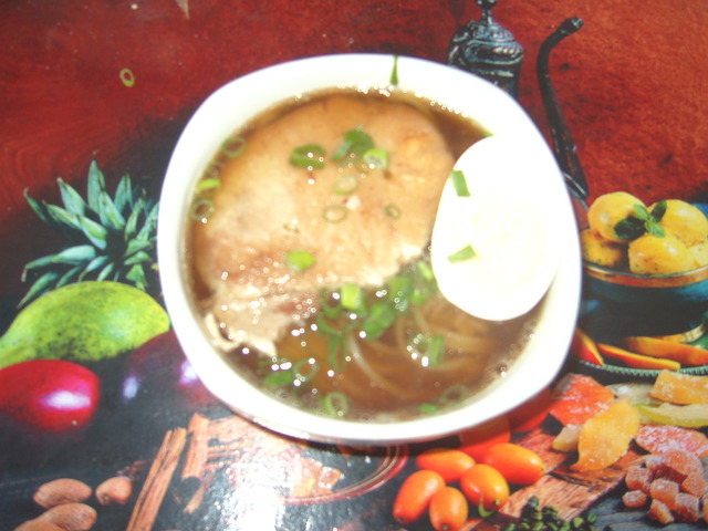 A bowl of soup with noodles in the bottom, and a thick slice of pork, a half boiled egg and very thin pieces of green onions on top. Since our bowl is small and can't fit much inside, the noodles got hidden beneath the other things and hardly appears in the photo.