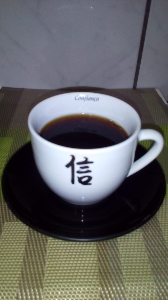 O café da Nova Guiné dentro de uma xícara que tem a palavra 'confiança' escrita em Japonês e em Português